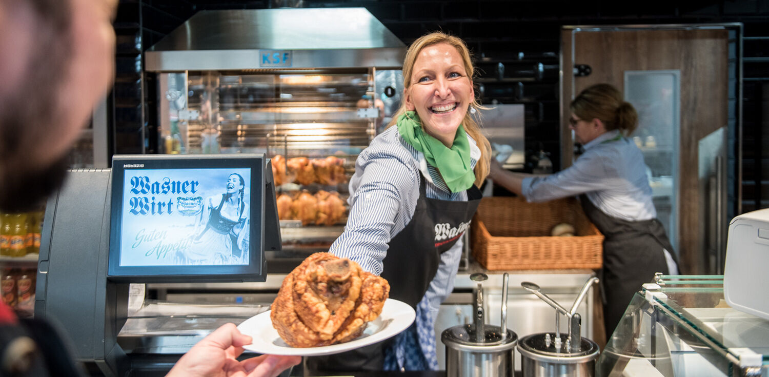 Eine Wasner Mitarbeiterin übergibt eine Haxe an einen Kunden